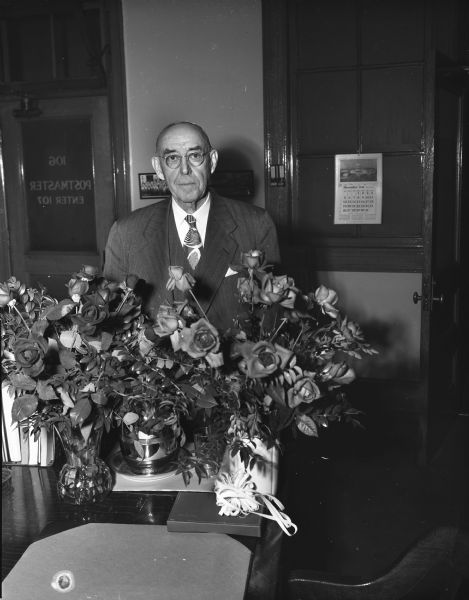 Portrait of Walter J. Hyland, retiring Madison postmaster, taken in his office behind a bouquet of roses presented to him by the postal clerks and supervisors.