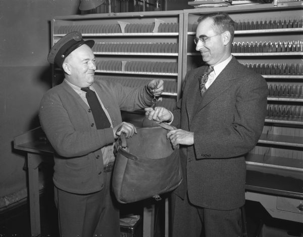 William R. Riley (left) turning in his mail carrier's sack and keys to Superintendent Leo Coyle of the University Avenue postal station.  Riley, with the postal system for 28 years and a carrier for 25, has been promoted to foreman of the city's letter carriers.