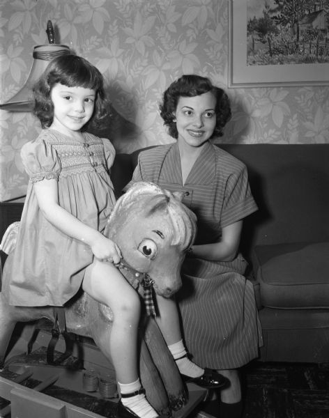 Mrs. Robert C. (Jean) McGuire, formerly of Oshhosh, and her daughter Jean Anne Shephard, on her hobby horse "Lulabelle," in their home at 4413 Winnequah Road. Jean Anne's father, the late Captain M. Shepard, was killed in Italy during World War II. The McGuires are newcomers to the area.