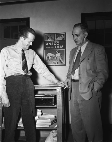 "Ken Ahrens (left), photographer at the Star Photo Shop, 924 Williamson Street, with R.E. Mattison, the shop owner, viewing the cash box which Ahrens prevented an armed bandit from robbing."