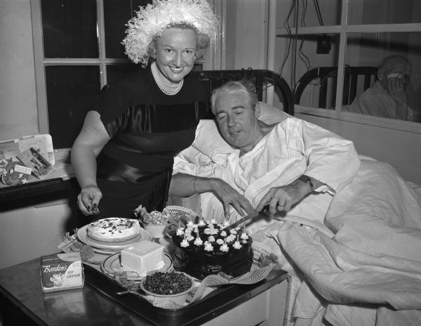 L.A. Toner,of Miami, Florida, is shown in his Wisconsin General hospital bed cutting his surprise birthday chocolate cake as his wife looks on. Mrs. Toner arranged the party and provided cake and sweets to all the patients on the sixth floor. "Mr. Toner, who underwent major surgery on Christmas Eve, is the steward of the Milwaukee Clipper ship in the summer time."