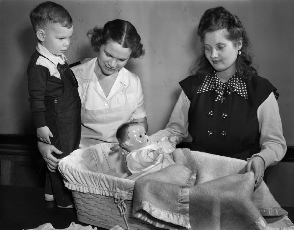 Mrs. Charles H. (Mary) Rogers, graduate nurse and instructor in the infant-care course at the Madison Vocational and Adult Education School, explaining certain phases of infant care to Mrs. Donald Allen, right, a GI bride who formerly resided in Athens, Greece. With Mrs. Rogers is her 21-month-old son, Danny, who has served as his mother's "guinea pig" in the class ever since he was a tiny baby.