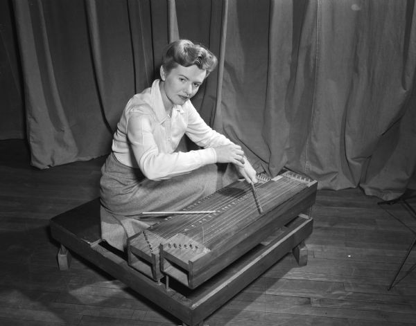 Shirley Genther, instructor in music theory and dance at the University of Wisconsin, with a musical instrument called a double canon, invented and constructed by Harry Partch, musical researcher who worked at the University in 1946 and 1947.