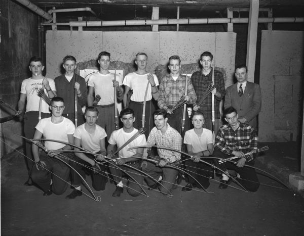 The West High School archery squad is defending its national title, which they have won two years in a row. Pictured, left to right, in the front row are: Charles Stumpf, Gene Fowler, Irv Johnson, Loel "Bud" Hahn, Harold Pierson, and Bill Rathbun. In the back row are Ronnie Babcock, Bob Walters, Bill Wolberg, Tom Erickson, Alan Bonsack, John Maloney, and coach Paul Olson.