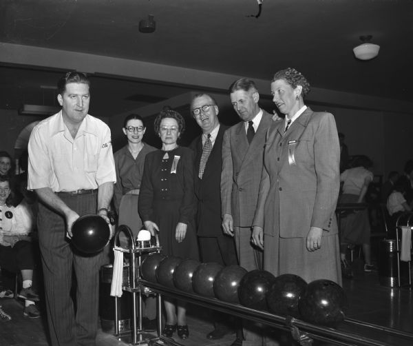Group portrait of persons participating in the opening ceremonies at the Plaza Alleys of the first women's state bowling tournament since 1931. Left to right: Connie Schwoegler, men's individual match game champion; Helen Zweck; Ruth Hoffman; Joseph "Roundy" Couglin; Madison City Manager Lenoard G. Howell, and Lucille Schoonmaker.