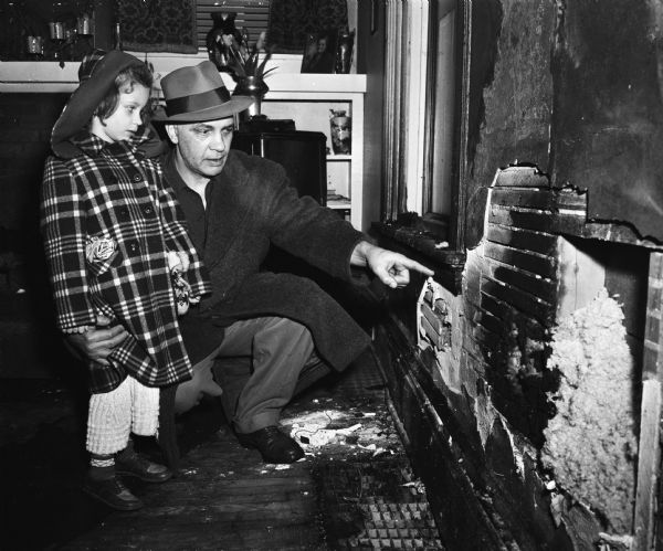 Ralph E. Mattison and his five-year-old daughter, Donna, examine the burned wall of their living room at 709 Orton Court.