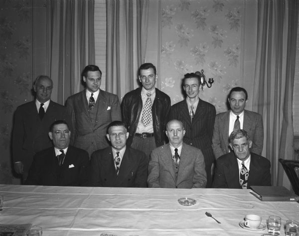 Group portrait of nine of the officials and managers of the Madison Industrial Baseball League. Front row, (L to R): Eddie Corcoran, West Side Businessmen Association manager; Glenn "Pat" Holmes, city recreation director & secretary of the Industrial Baseball League Commission; Duane Bowman, Commission President; and Eddie Lenahan, Commission vice-President. Back row, (L to R): Willis Jones, Breese Stevens Field manager; Stan Stavrum, Oscar Mayer manager; Ed Heinricks, Bowman Dairy manager; Lew Cornellus, Gardner Bakery manager; Francis "Bonnie" Ryan, city recreation and league publicity writer.