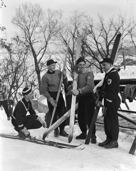 Four ski "jumpers" are posed on a hill with Lake Mendota behind them. They are, from left to right: Allen Bushnell, Wally Alcumbrac, Bill Bradley, and Don Critton, all of Madison. They will participate in the 17th annual intercollegiate ski meet sponsored by the Wisconsin Hoofers' club as part of the University of Wisconsin Winter Carnival week. The ski jumping tournament took place on campus at Muir Knoll on the north side of Bascom Hill.