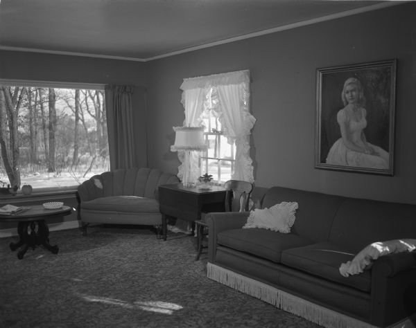 View of the living room of the Carl A. Anderson home on East McKinley Street. A portrait of the Anderson's daughter, Mrs. Owen Klongland, hangs above the sofa. It was done by Madison painter A.N. Colt of Madison. A large picture window has a view of trees and snow.