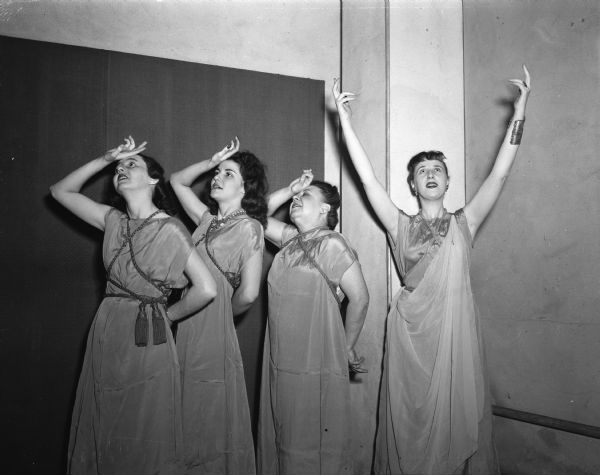 Four women in costume, posing in a scene from "Lyristrata"; part of a comedy program, "A Combine of Comedy" produced by Phi Beta in the play circle of the Memorial Union. Left to right: Jean Kanable, Richland Center; Mrs Joseph Klein, 3522 Lucia Crest; Mrs. John E. (Frances) Dudley Jr., 4162 Cherokee Drive; and Geraldine Ryan, director of the Madison Civic Theater, enacting the title role.