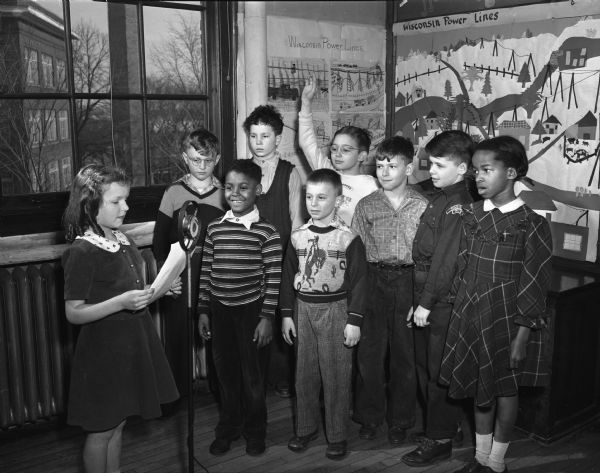 Third and fourth graders from Longfellow school putting on a "quiz show" about electricity and lights that they have been studying. Joanne Tewalt (left) is reading questions to third graders Floyd Smith and Robert Behrend in the front row, and Billy Holstein, Thomas Wills, and Martha Freeman, fourth graders in the front row. In the back row are fourth graders Ronald Weinstein, Thomas Goodell, and Bobby Cuccia.