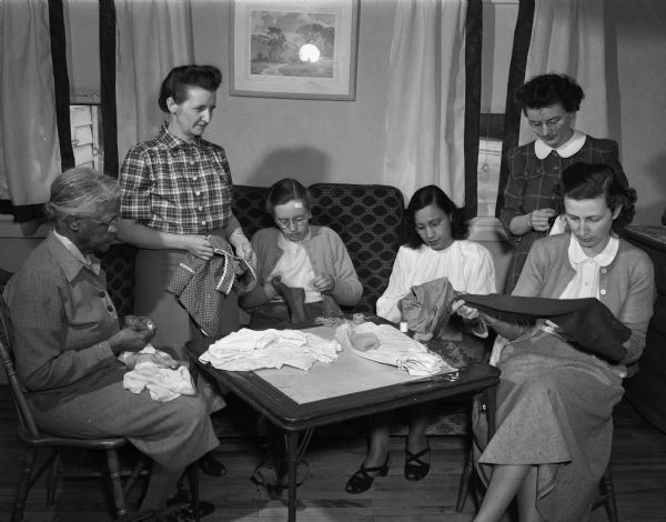 A group of women mending clothes for the Quakers' relief clothing project at one of their regular Tuesday morning sessions at the home of Mrs. Hilton E. (Lillian) Hanna, 39 North Randall Avenue. From left to right are Mrs. Grace Bell, Mrs. Hanna, Mrs. Eugene Ackerman, Mrs. David H. (Mary) Simms, Mrs. Walter K. (Mabel) Johnson, and Mrs. Stephen C. (Megan) Smith.