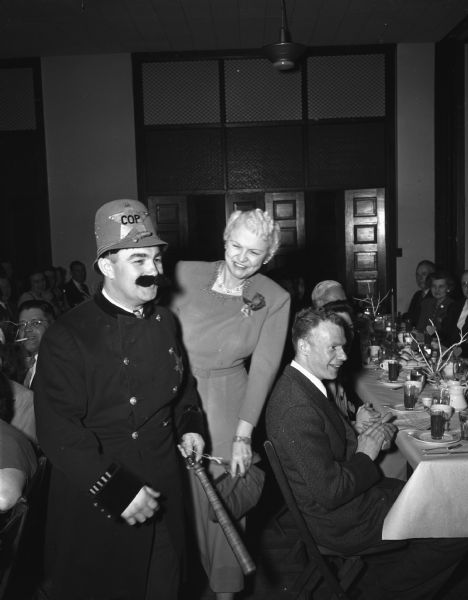 Harold Lautz, sergeant-at-arms for the annual Lutheran Men's Club "Sweetheart's Dinner" held in the Lutheran Memorial Church, 1021 University Avenue. Mr. Lutz is dressed in costume as an old-time police officer. Mrs. Oscar (Mary) Rennebohm is standing next to him.