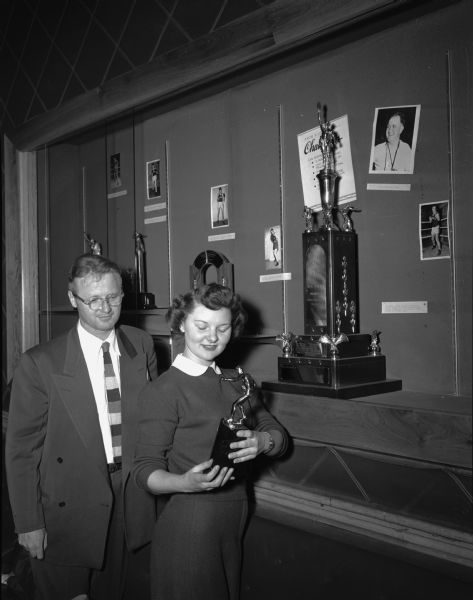 Jerry Erdahl, left, night manager of the Memorial Union, and Fern Anderson, chairman of the Union Trophy Room, discuss the placement of the last trophy in the exhibit of University of Wisconsin boxing trophies and pictures.
