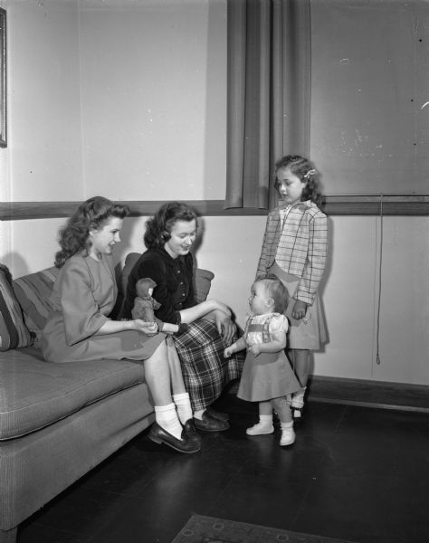 West High School pupils Muriel Showers and Anna Pronin watch Pamela Showers, 15 months, and Joan Gmeinder, 7, model two of the outfits that clothing students at West High School have remodeled for a Displaced Persons camp in Germany. Both Showers and Pronin stayed at the Schlessheim-Feldmoching Displaced Persons Camp near Munich, Germany.