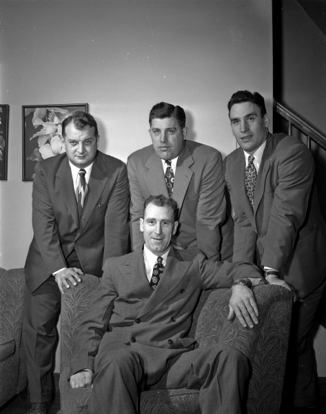 From left to right, Paul Shaw, Milt Bruhn, and Bob O'Dell, varsity assistant coaches, stand behind a seated Ivy Williamson, head football coach, while posing for a portrait.  All of the men are wearing suits and ties.