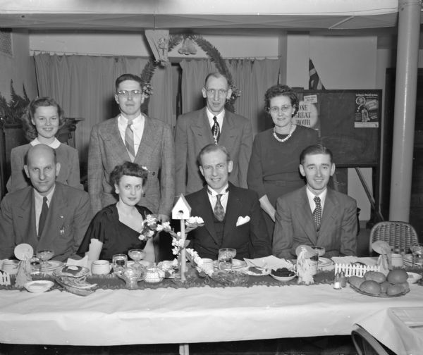 Group portrait of Zion Evangelical Lutheran church members posed at banquet table at 247 Division street.  Seated left to right are: Francis Goold, congregation president; Olga Splett, choir director and wife of the pastor; pastor F. Paul Splett; and Carl Rochlus, scoutmaster.  Standing in the back row, left to right, are: Jean LeFebvre, president of the Junior Luther League; Rodney Erickson, president of the Senior Luther League; Louis Knickmeyer, chief usher and Idella Knickmeyer, president of the Ladies Aid.