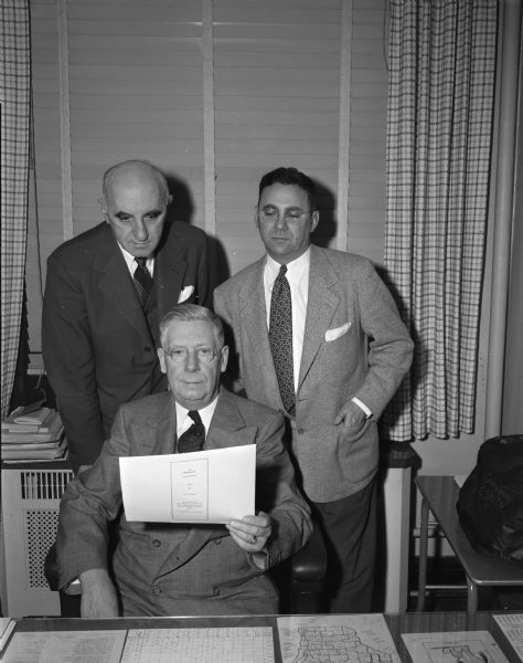 Shown examining a "safe-driving agreement" for youthful drivers and their parents are the men who are in charge of the statewide distribution of this aid to accident prevention. Pictured from left to right are: R.C. Salisbury, director of the safety division, motor vehicle department; Ralph Hult, Madison automobile dealer and chairman of the safety committee of the Wisconsin Automotive Trades assn.; and Louis Milan, executive secretary of the Wisconsin Automotive Trades Assn.