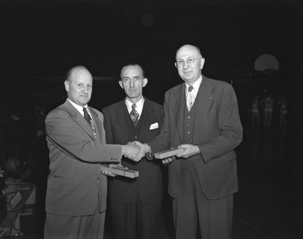 Guy Sundt (left) and Paul F. Neverman (right) were paid tribute for their quarter of a century of service to the WIAA state high school basketball tournament. Charles W. Wetmore, Sun Prairie principal and president of the WIAA Board of Control is presenting the two with gold watches.
