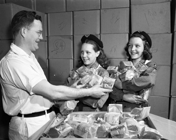 Judith Engel and Joanne Fraililng, Girl Scouts from Troop 46 at East Jr. High School, receiving cookies from Reidar Strand. The Strand Bakery, 2007 Atwood Avenue, baked the cookies for the Girl Scouts for many years.