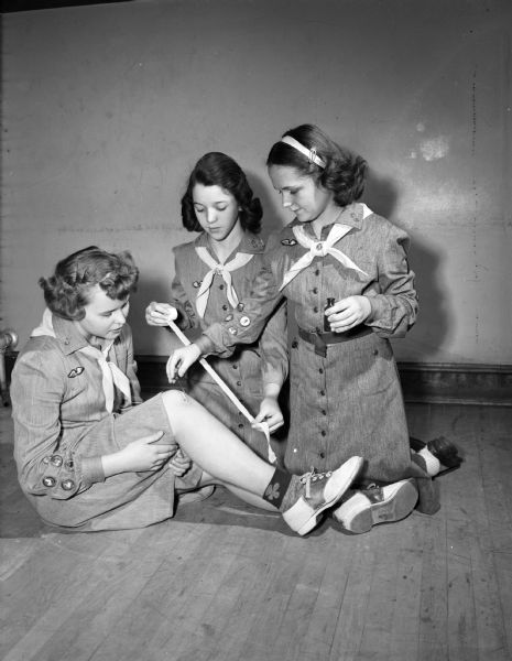 Members of Troop 46, East Jr. High School, Kay Greudenberg is being cared for by Helen Brigham, and Patsy Stoker, who are practicing first aid. First Aid is one of the required projects for the Girl Scouts to master.