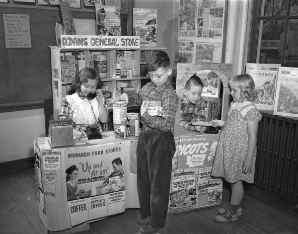 Four third graders in their general store set up in their classroom. At left clerk Amy Jo Voges takes a grocery order while Clare Sampley portrays a patient customer. On the right postmaster Tom Brown accepts a letter from Nancy Hovland.