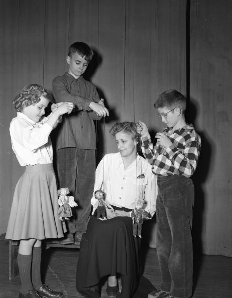 Sara Reznichek watching three Marquette school fourth graders practice for their puppet show "Heidi" during the school's family fun night. The students, left to right, are Joan Herreid, Richard Reznichek, and Carl Fosmark.