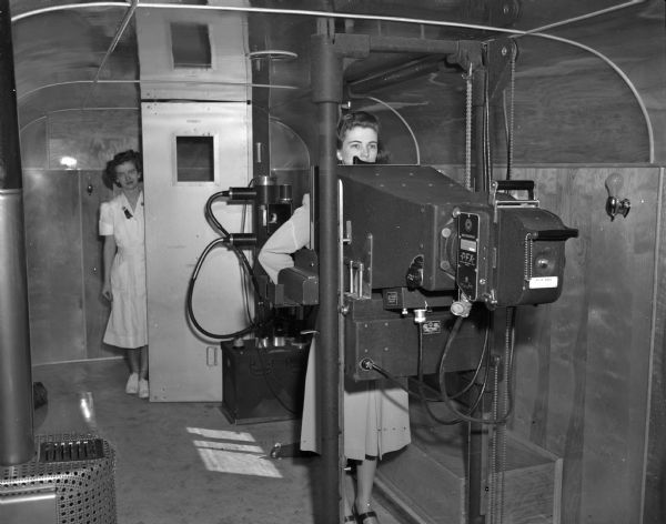 Interior of trailer with portable X-ray machine. Jean Gibbons, X-ray technician, is shown with unidentified woman getting an X-ray.