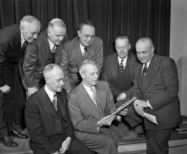 Group portrait of seven men involved in the Bethel Lutheran Church campaign to raise $100,000 in 100 weeks for a new Sunday school building. Seated left to right are: the Rev. F.I. Schmidt, pastor of the church; and Harold B. Shier, chairman of the finance committee.  Standing left to right are: John Ellestad, Basil I. Peterson, George Johnson, L.J. Larson, and O.O. Lokken, all members of either the finance committee or the building planning committee.