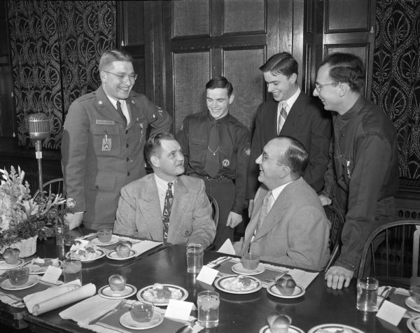 Two of the 170 scouts from all over Wisconsin conversing with members of the University of Wisconsin service fraternity, Alpha Phi Omega, at a banquet in the Memorial Union. Seated are: LeRoy Arndt, left, field executive of the Four Lakes council; and Jim Morrow, Ottuma, Iowa, fraternity member. Standing, left to right, are: Richard Hile, Madison, general chairman of the event for the fraternity; Edward Douglas, Waukesha scout; George Melcher, Eau Claire, fraternity member; and Dave Mueller, Waukesha scout.