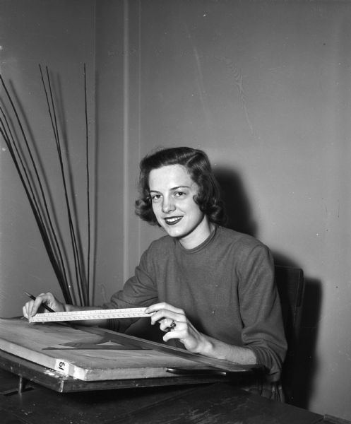 Pictured is Dorothy Worel, Manitowoc, a home economics student at the University of Wisconsin, planning a kitchen for one of her classes. Ms. Worel, who is an Alpha Phi pledge, is a member of  the "court of honor" for the UW Military Ball, one of six co-eds chosen for their attractiveness and charm.