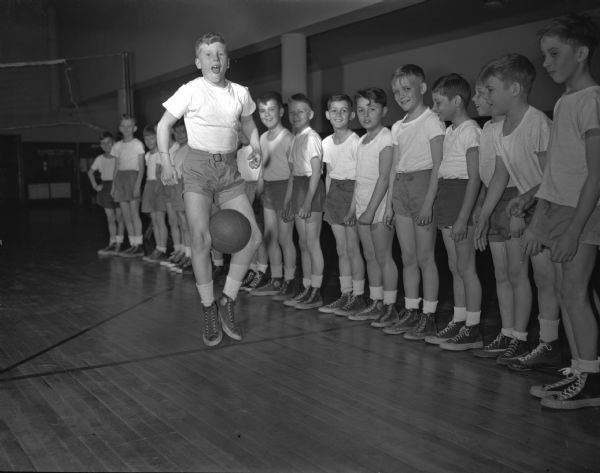 Charles Holtz is shown completing a relay race hopping with a ball between his knees as other boys look on.