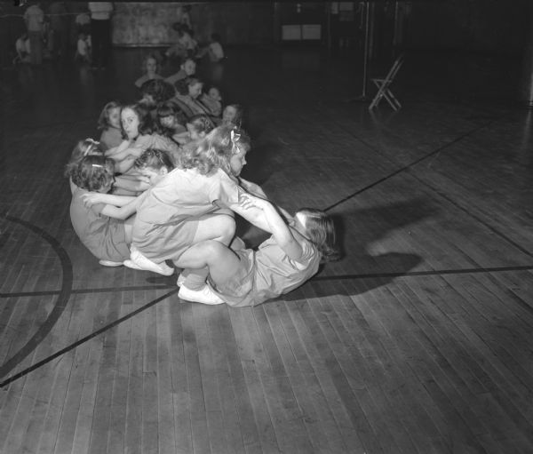 Several young girls are shown performing their "push-me, pull-you" exercise. Nearest the camera are Mary Holtz and Phyllis Garland. Then come Barbara Drake and Sharon Bender, Lois Ellefsson and Alberta Bauman, and Elaine Bricker and Gwen Engel.