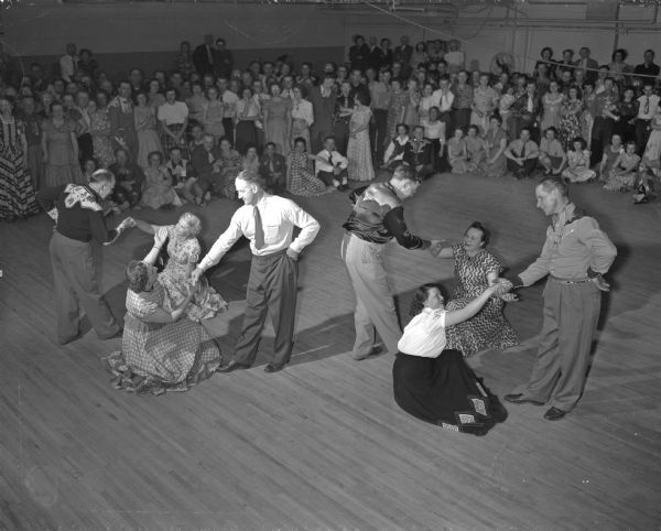 Four pairs of square dancers perform as many fans watch from the side at the Madison Community center.