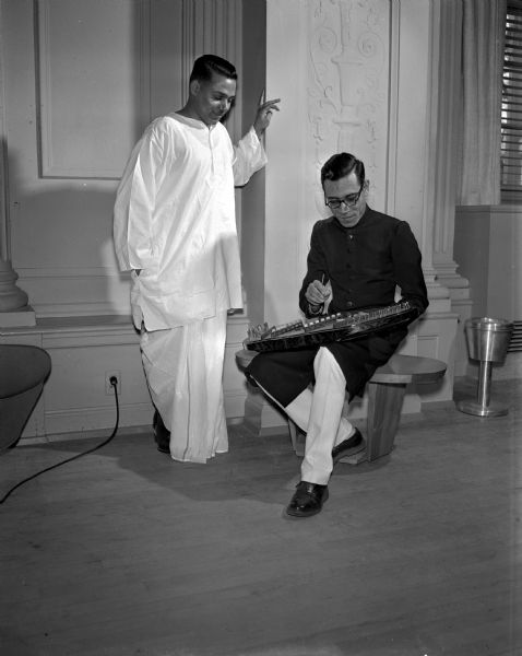 Indrapal Verma of Aligarh, India, watches Mohammed Hanif Khan of Karachi, Pakistan, attempting to play an Oriental "butterfly," a musical instrument brought to the University of Wisconsin International Club Ball by a Chinese student.
