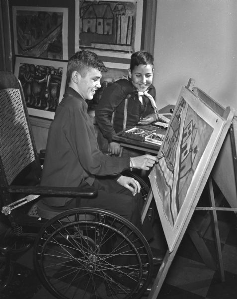 Richard Johns of Janesville puts the finishing touches on a painting while seated in a wheelchair at the orthopedic department at Washington School, 545 West Dayton Street. Looking on is John Grapses of Madison.