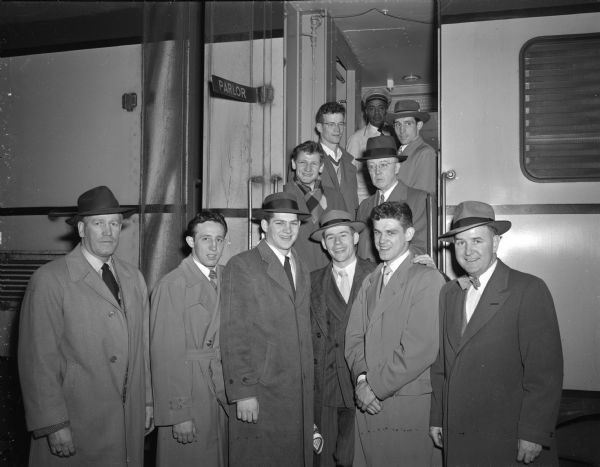 Preparing to depart by train for the forthcoming NCAA boxing meet are University of Wisconsin national boxing team defending champions and their coaching staff. Left to right from the front are: Asst. Coach Vern Woodward, Dwaine Dickinson, Bobby Ranck, Manager Ray Hogue, John Lendenski, and Coach John Walsh. Standing on the steps left to right are: first row, Steve Gremban and team physician, Dr. John Bentley; second row, James "Red" Sreenan and Don Dickinson.