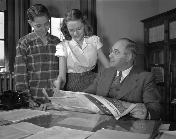 A.F. Ketterer, principal of Franklin elementary school is at his desk looking over <I>Wisconsin State Journal<i> Badger Spelling Bee material with two of his students, Charles Willadsen, at left, and Pat Taylor, center, both spelling bee champions. Mr. Ketterer is a member of the 1949 Madison Community Chest budget committee.