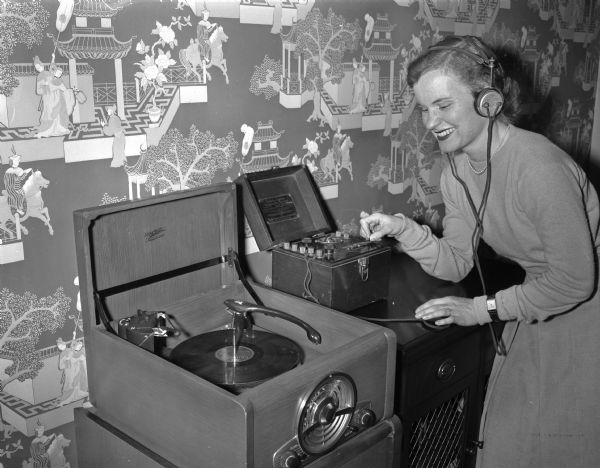 Barbara Lampert, a University of Wisconsin senior, tunes a 1921 model radio next to her new radio-record player at the Madison Home Appliance and Radio Show in the East High School gymnasium.