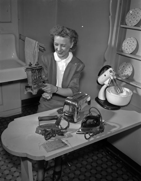 Dorothy Lorenzen looks at several small kitchen appliances while she holds one of the earliest electric toasters at the Madison Home Appliance and Radio Show in the East High School gymnasium.