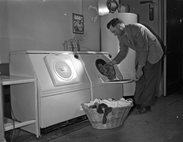 Charles M. Mickelson is loading an automatic washer, with the companion dryer at the left, at the Madison Home Appliance and Radio Show in the East High School gymnasium.