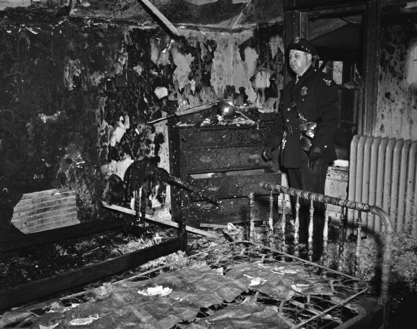 Police Officer Walter E. Randall looking at fire damage to the bedroom of Dorothy Meager, 111 North Blair Street.