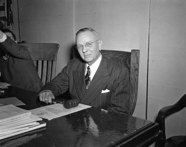 Ernst J. Deppe of Marshall sits behind a desk covered in papers and is holding a gavel. He was narrowly elected Dane County board chairman, 42 to 40, over Prof. Robert H. Gerry, Madison.