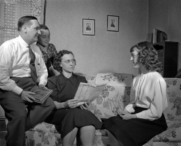 Wrenn O'Connell and his wife Margaret practice for the Badger State Spelling Bee with their daughter, Margaret, while sitting on a living room couch. Margaret's brother, Billy, is standing behind them.