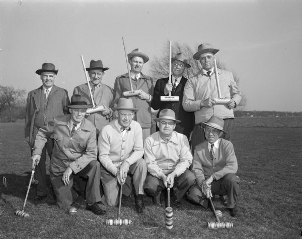 Group portrait of two east side men's croquet teams, holding their mallets. Standing, left to right: Tommy Olson, referee; Wally Hoffman; Ole Olson; Marvin Smithback; and Lars Landness.  Kneeling are: Marshall Brown, H.J. Loftsgordon, Al Larson and John Niles.