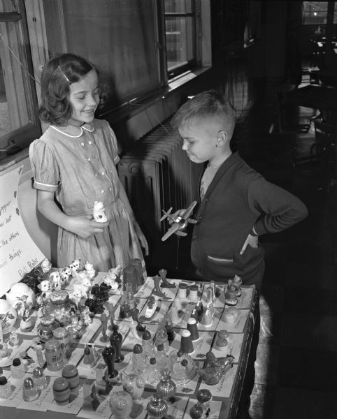 Pat Rohr, 16 North Bassett Street, standing next to her salt and pepper shaker collection at the Washington School Hobby Show. Stan Fix, holding a model airplane, views her collection.
