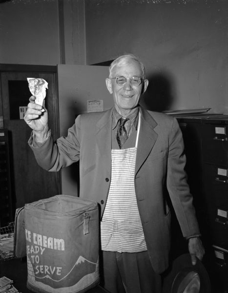 A man holds up an ice cream cone while standing in front of an insulated container labeled "Ready to Serve".