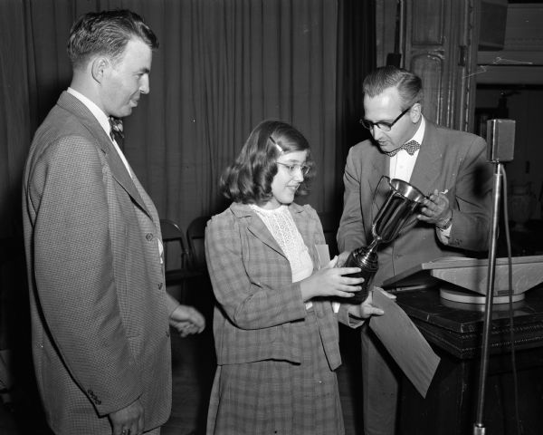 Roy Matson, <i>Wisconsin State Journal</i> editor, standing to the right and presenting a championship trophy to Charlotte Kreul of Fennimore, Wisconsin. Warren R. Jollymore, in charge of the spelling bee, is standing on the left.