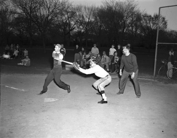Action in a Mendota League softball game in Vilas Park. The batter is Bob Olson of Philgas. The catcher is Charcoal Grill's Armstrong. The umpire is Vito Schiro.