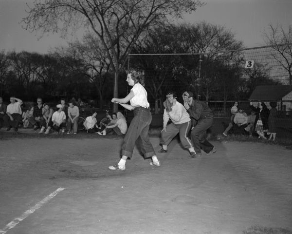 Carroll Becker of Norberg Electric batting in a Madison women's softball league game. The umpire is Charlie Pendergast.